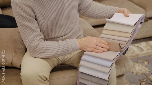 Man selecting fabric swatches for sofa upholstery, choosing textile samples for interior design and home renovation