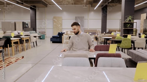 Man examining a chair and table set in a large furniture store, choosing new pieces for home interior design
