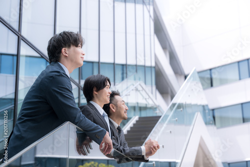 Canvastavla 屋外のビル背景で未来を見据え笑顔で語る会社のビジネスマンチームの成長と挑戦　プロジェクトの成功などのポジティブ前向き上司、若手の部下をなど3人チームのイメージ上
