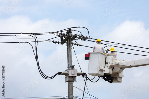 Electric utility workers repair and install high voltage power lines from a bucket truck, highlighting electrical maintenance, infrastructure service, safety procedures, and skilled labor.