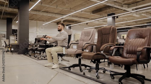 Person trying out an office chair in a furniture store. Choosing comfortable office seating for workspace and productivity. Man imaging how he is using virtual keyboard or laptop