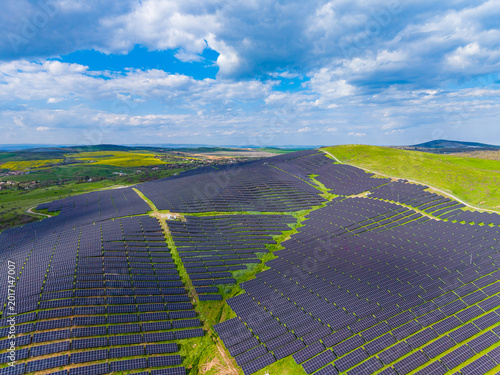 Solar panels spread across a hillside in a rural area under a blue sky with clouds, showing a commitment to renewable energy in an open landscape