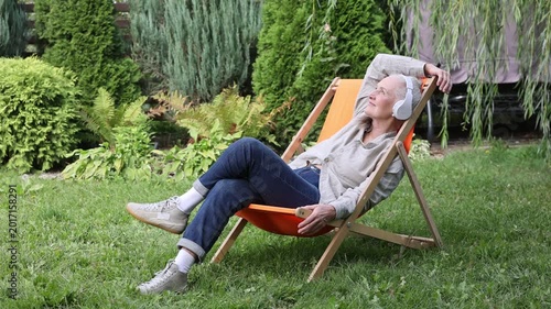 lifestyle portrait smiling senior woman with gray hair in headphones relaxes sitting on a chair in the garden . spends time in nature. Audio healing. Mindfulness and feel-good moments.	
