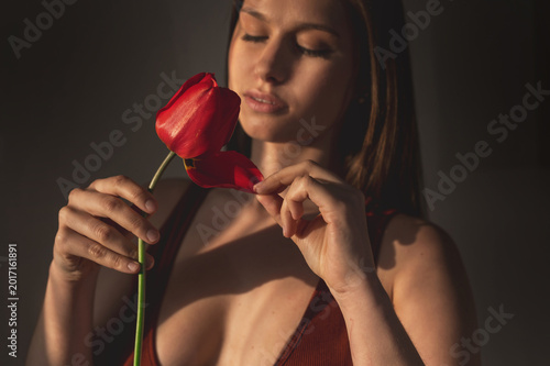 Schilderij op canvas Cinematic portrait of an attractive young woman holding a red tulip
