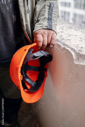Foto Close-up of a dirty, calloused worker's hand firmly holding a bright orange safety helmet resting on the edge of an unfinished concrete windowsill