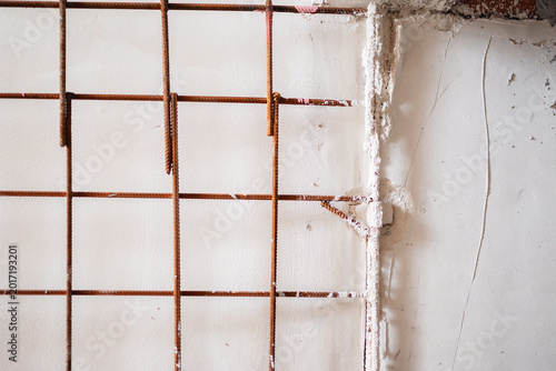 Canvas Print Rusty steel rebar mesh embedded into a rough white plaster wall acting as a makeshift barrier or structural reinforcement at an active construction site