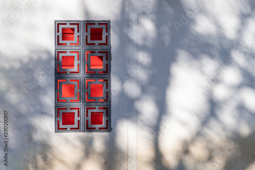 Exterior view of oriental grey and red Chinese style windows on white wall of resident building. The sunlight shines through trees and causes shadows on Chinese style house.