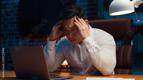 Foto Fatigued unhappy Asian mature business man working laptop in evening office at n
