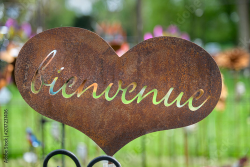 Rusty heart shaped welcome sign with French greeting in a blurred garden background