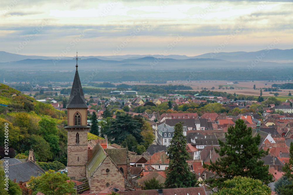 Fototapeta premium Panoramic aerial view of Ribeauville town with Saint Gregoire church tower. Scenic autumn landscape of Alsace wine region with red roofs and Vosges mountains, France.