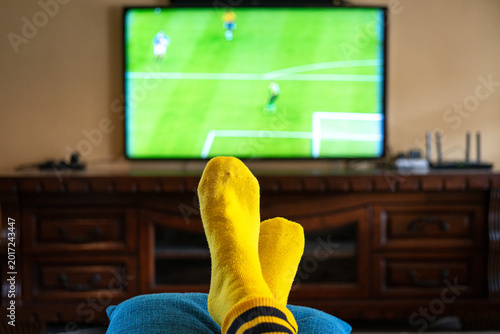 Person Watching Soccer Game on Television, at home feet up wearing yellow socks. 