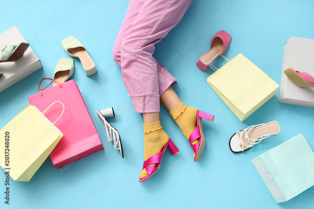 Naklejka premium Legs of young woman with different stylish high heel sandals and shopping bags on blue background