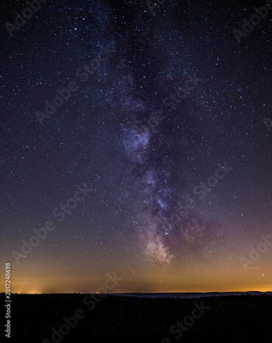 Milky Way galaxy rising over Black Forest silhouette with city light glow on horizon, astrophotography Germany