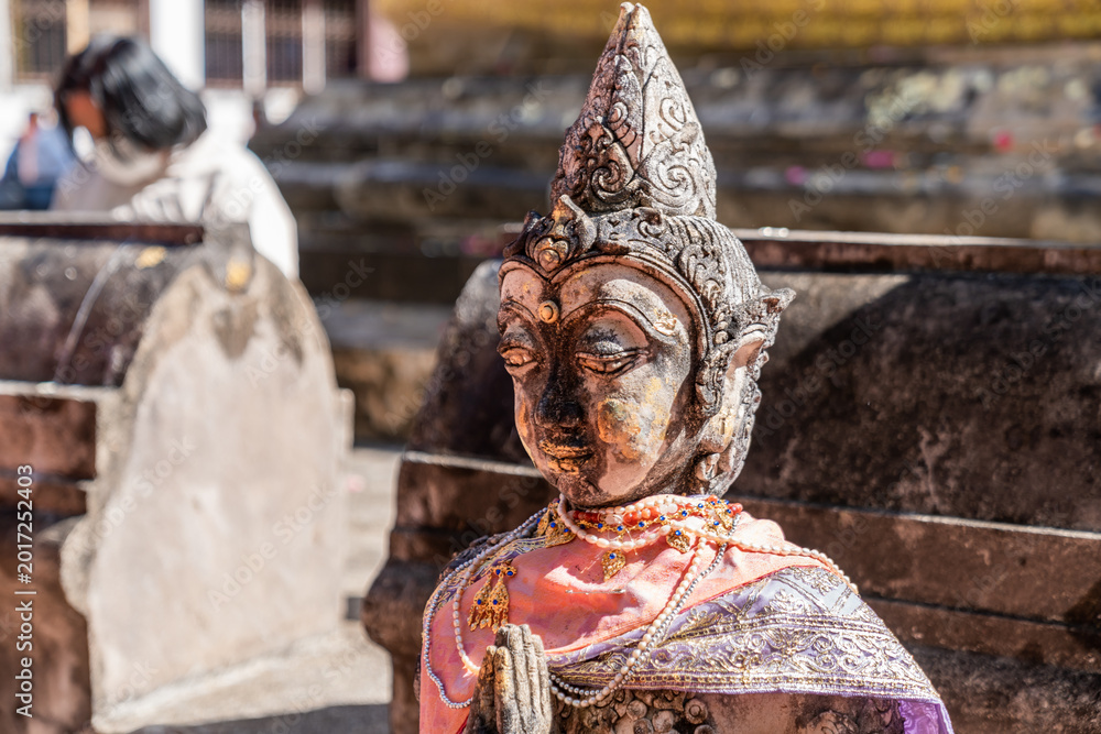 Fototapeta premium Weathered female guardian figure stands within a sacred temple site surrounded by historic stone structures and cultural heritage architecture.