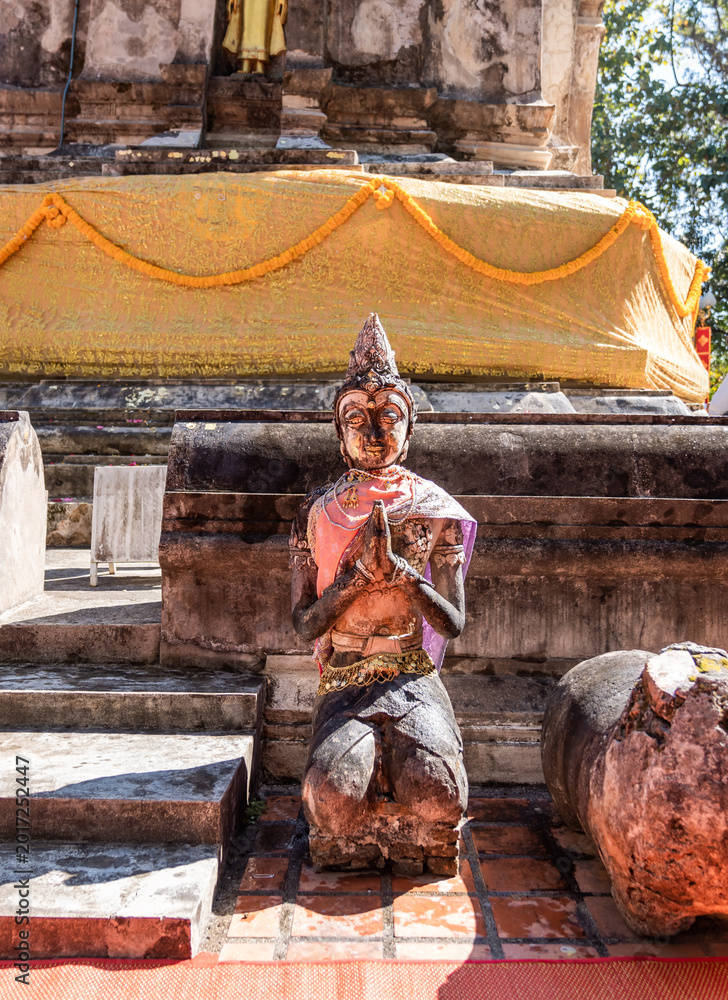 Fototapeta premium Weathered female guardian figure stands within a sacred temple site surrounded by historic stone structures and cultural heritage architecture.