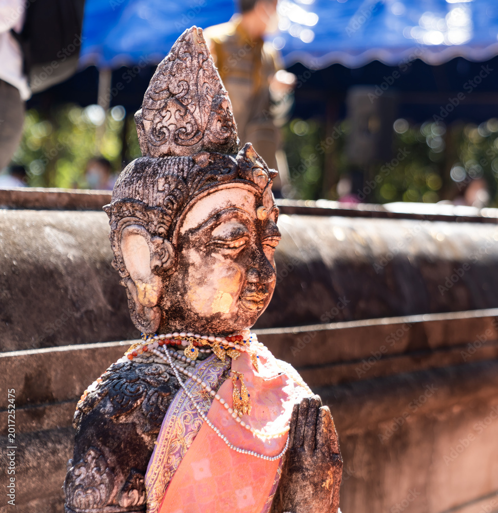 Fototapeta premium Weathered female guardian figure stands within a sacred temple site surrounded by historic stone structures and cultural heritage architecture.