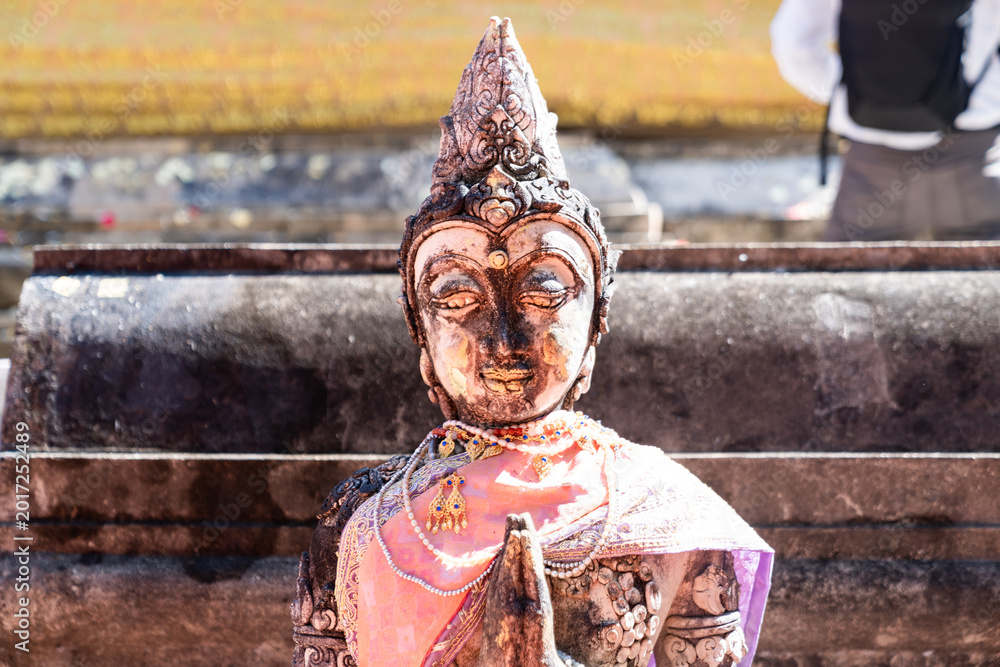 Fototapeta premium Weathered female guardian figure stands within a sacred temple site surrounded by historic stone structures and cultural heritage architecture.
