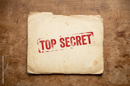 old file folder with top secret stamp containing classified confidential information document on desk