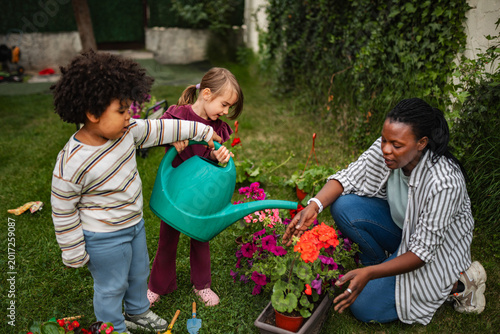 Canvas-taulu Children and adult woman watering flowers in garden