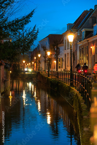 Dutch canal at blue hour with row of house on the side, people cycling on the street with lighting on, Amersfoort, Netherlands, European lifestyle