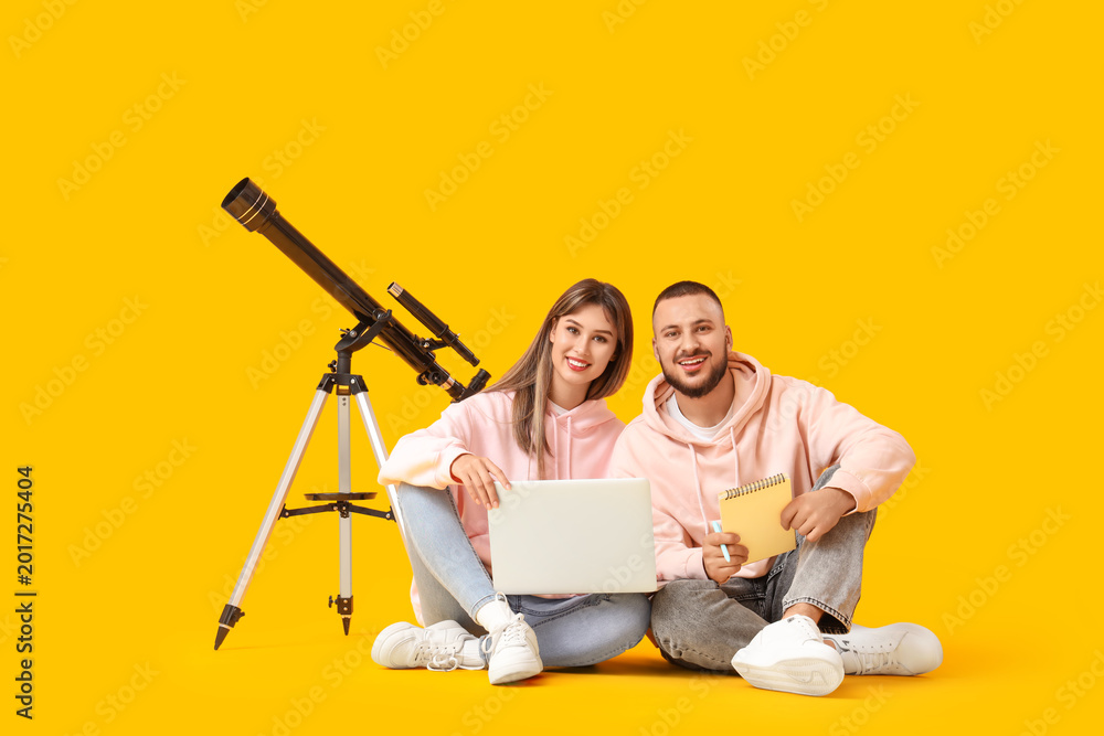 Fototapeta premium Young couple with laptop and telescope sitting on yellow background