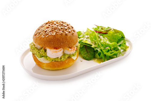 Shrimp sandwich with salad served on a white plate in a well-lit kitchen