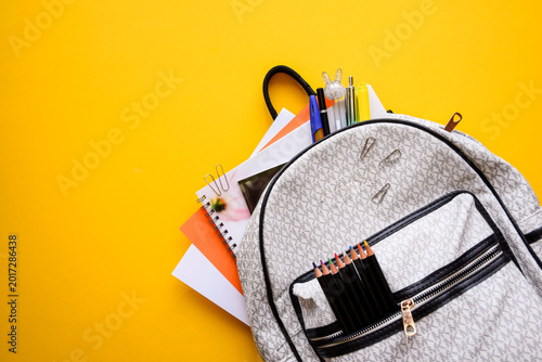 School Backpack with Colored Pencil Set Notebooks and Pens on Yellow Background with Copy Space