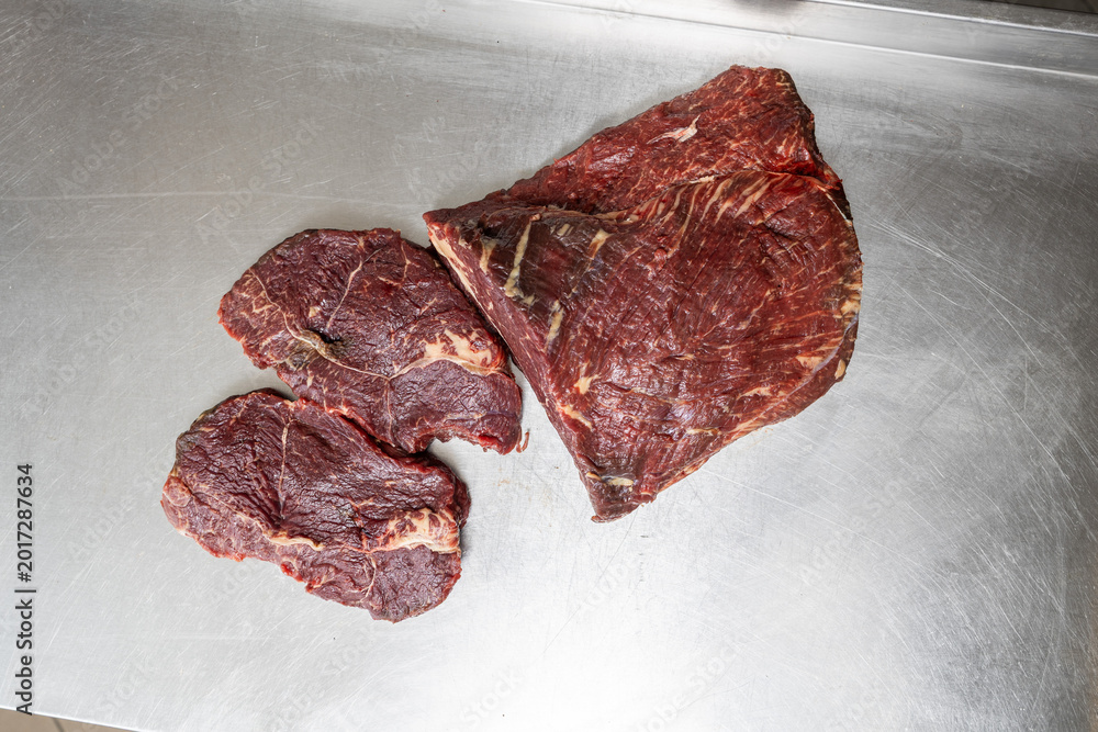 Fototapeta premium Top view of raw beef primal cut and steaks on stainless steel
