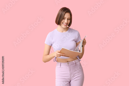 Young woman in stylish t-shirt holding fashion magazine on pink background