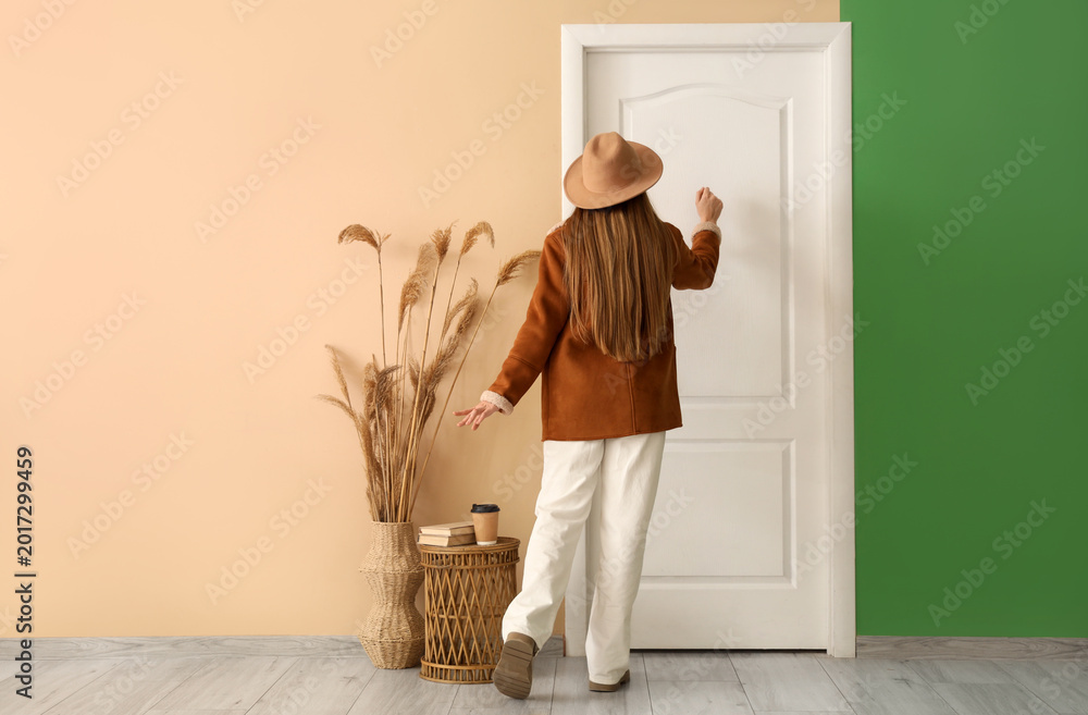Fototapeta premium Young woman in autumn outfit standing knocking on door at home