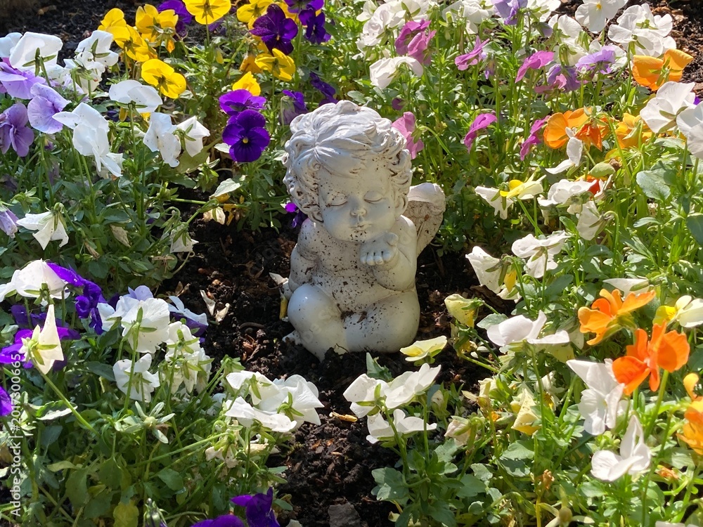 Obraz premium Kleiner Engel zwischen Blumen auf dem Friedhof in der Sonne