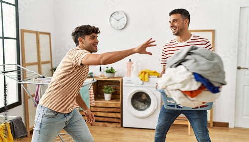 Laughing men wearing striped T-shirts and jeans handling laundry in home laundry room, with basket