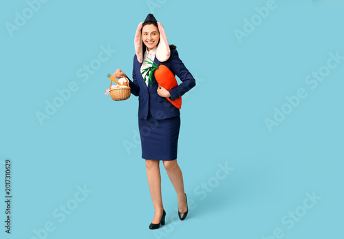 Happy stewardess in bunny ears with Easter basket and toy carrot on blue back...