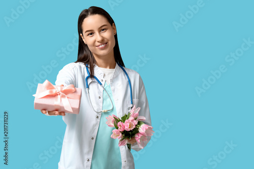 Female doctor with pink tulips and gift box on blue background. Women's Day c...