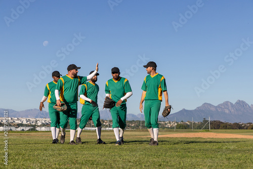 Photos Male baseball teammates walking in outfield, giving high five, wearing green jer