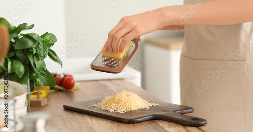 Young woman grating cheese ...