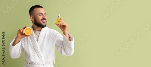 Foto Young man holding bottle of cosmetic serum and orange on green background with s