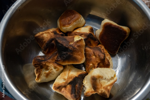several small square yeast buns with dark charred crusts sitting inside large stainless steel mixing bowl after unsuccessful baking process.