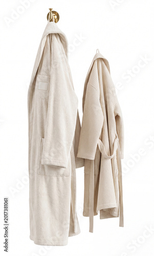 Two cream bathrobes, one plush terrycloth and one waffle-knit, with hoods and ties, hanging on hooks isolated on a white background.