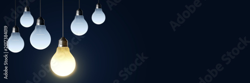 Fotografie Glowing lightbulb among dim hanging bulbs on dark background representing creative idea, innovation concept, clean modern design and abstract symbol of inspiration