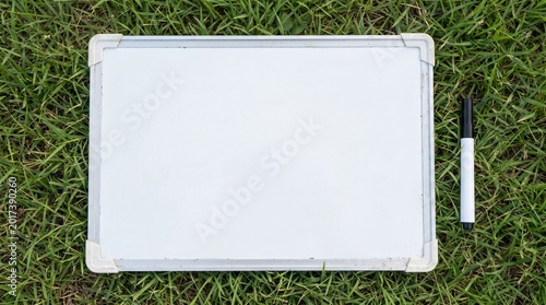 Blank white coaching whiteboard and black marker on natural green grass concept of sports strategy planning coaching and education