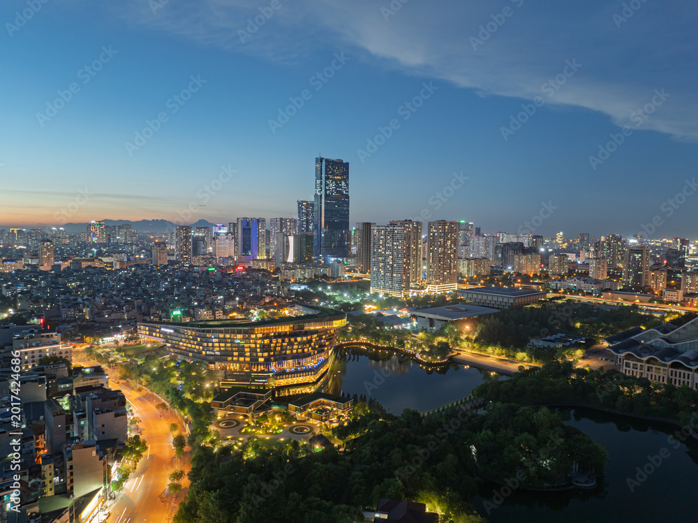 Fototapeta premium Twilight aerial panorama of modern Hanoi skyline with illuminated buildings, lakes, and vibrant urban districts during blue hour.