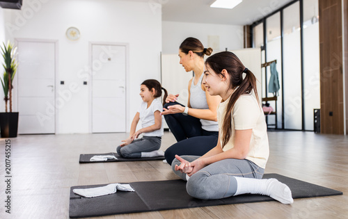 Foto Female coach performing corrective exercises with two young girls on mats in studio