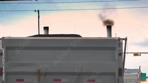 Close-up of heavy black smoke billowing from dual vertical exhaust stacks of a white dump truck.