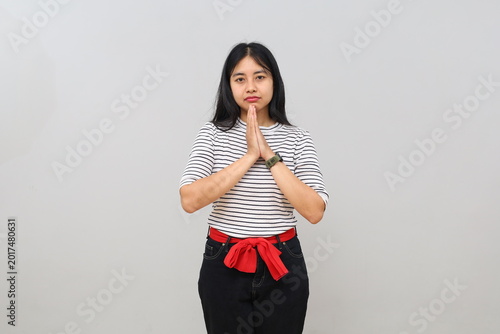 Canvastavla A young woman puts her hands together in front of her chest in a pleading expression, showing hope, gratitude, or asking for help, a prayer gesture, standing alone on a white background