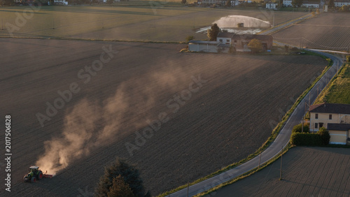 Konstfotografi Tractor working dusty Po Valley field at sunset during drought, modern agribusin