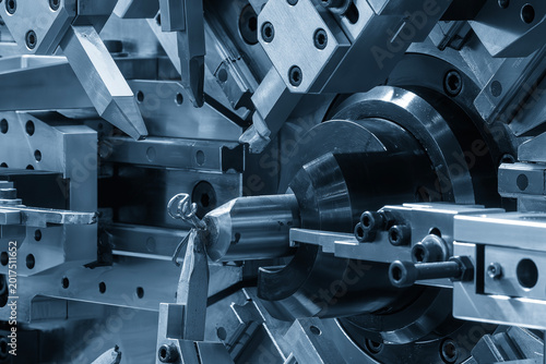 High-speed automatic bending machine forming a metal wire coil spring in a blue-toned industrial scene.