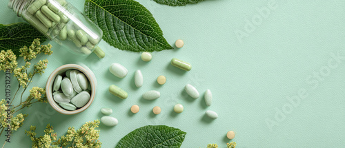 Assorted herbal capsules and tablets with green leaves and flowers on a pastel green background, evoking natural wellness and health concepts.