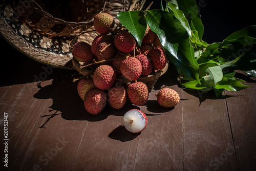 Tableau sur toile Fresh red lychees with green leaves in a wicker basket on a wooden table