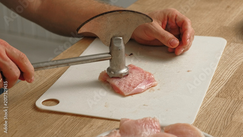 Fotografie Person using meat tenderizer on raw chicken
